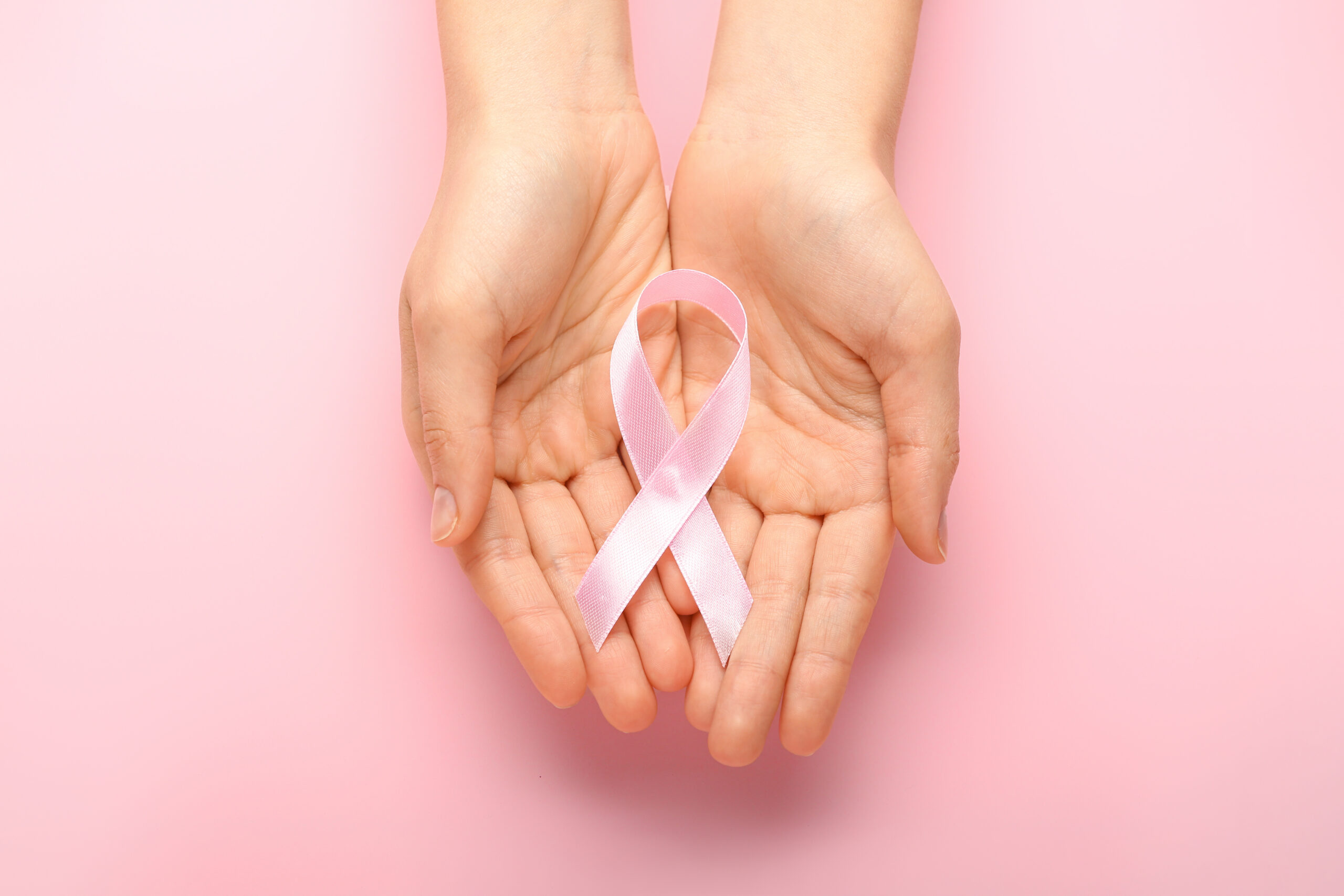Female hands with pink ribbons on color background. Cancer awareness concept